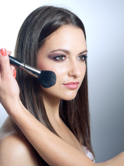 A makeup artist applies blush to a woman's face.