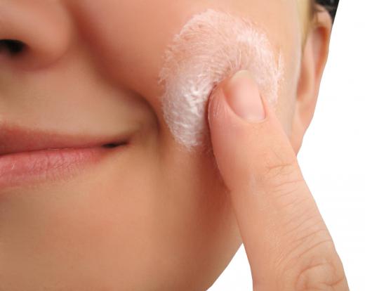 A woman applying cream to her face to remove a blemish.