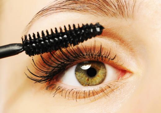 A woman applying mascara, a type of cosmetic.